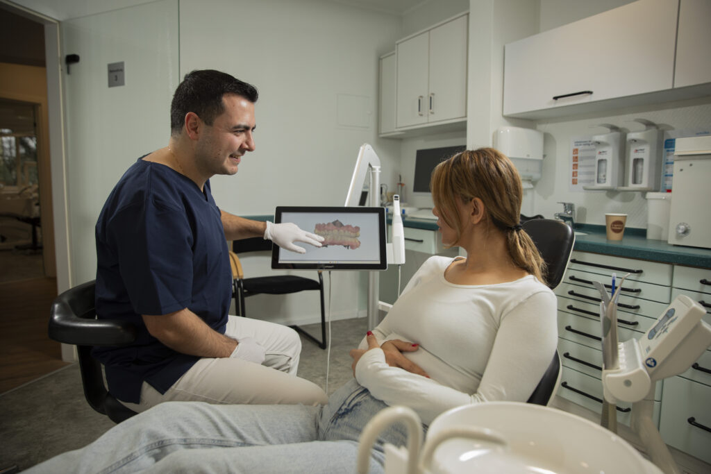 Ein Zahnarzt zeigt einer lächelnden Frau auf einem Tablet das Bild eines Kiefers