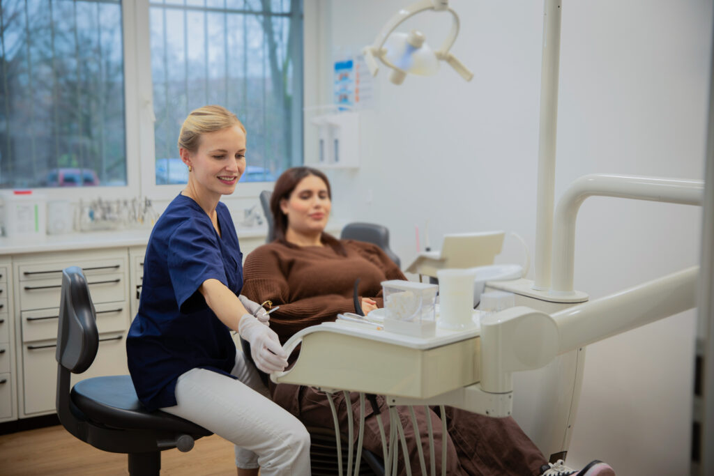 Eine blonde Zahnärztin mit freundlichem Lächeln behandelt eine entspannt wirkende Patientin in moderner Praxis